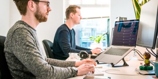 Photo of two men at their desks, looking at their computer screens.